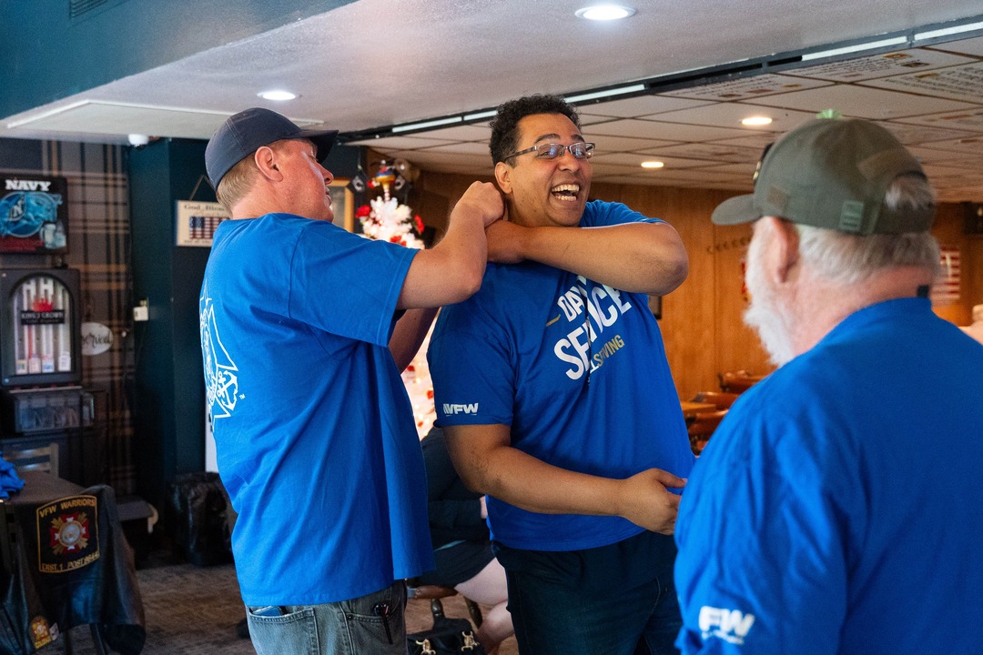 Two gentlemen in blue shirts, one attaching a pin to the other's shoulder.