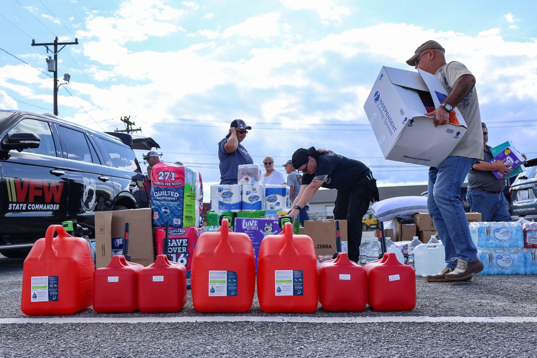 Group of people gathering supplies of gas cans, toilet paper, diapers, and other assorted essentials for donation purposes.