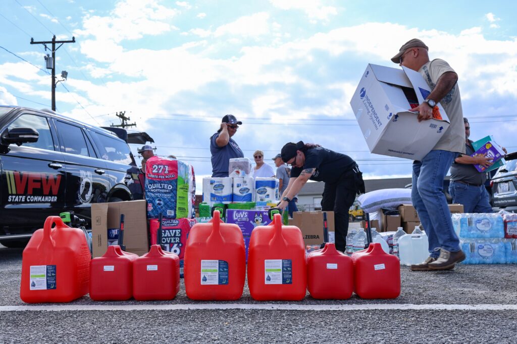 Grupo de personas reuniendo suministros de bidones de gasolina, papel higiénico, pañales y otros artículos esenciales variados con fines de donación.