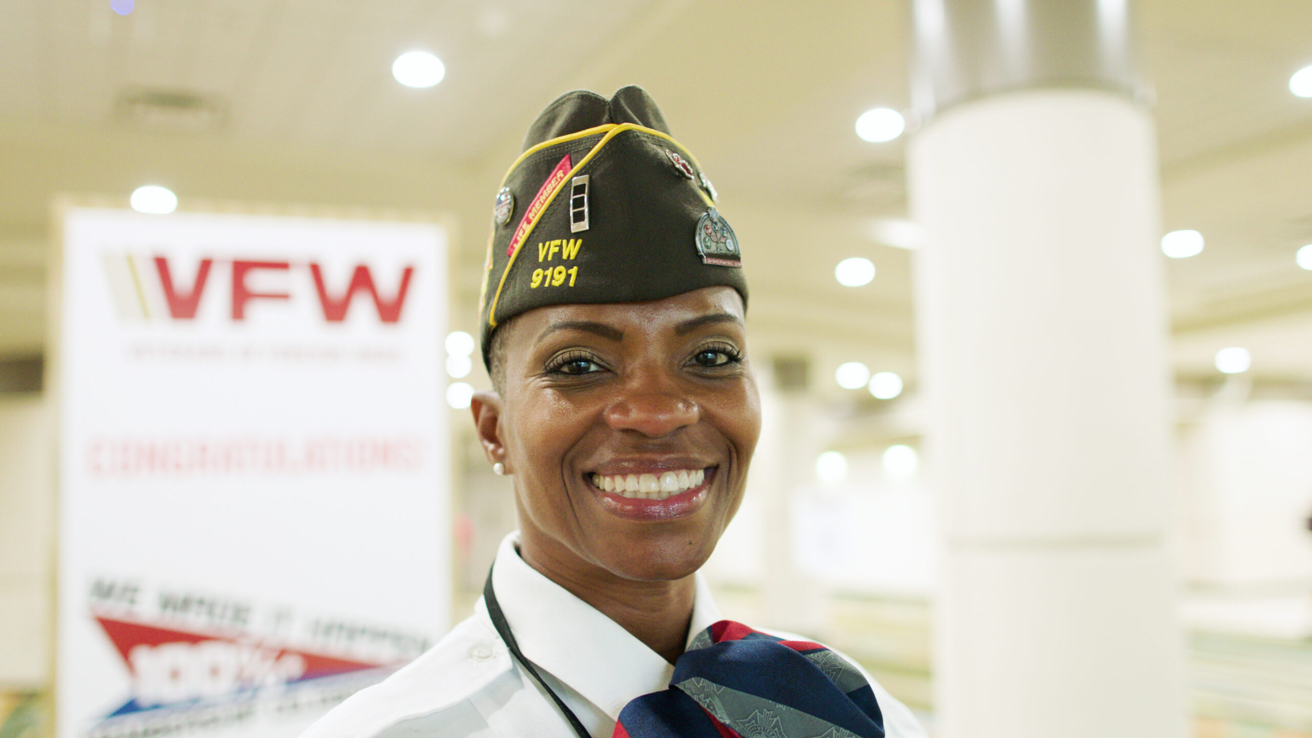 Female soldier with decorated hat smiling with VFW sign in the background.