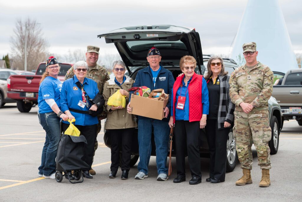 Group of people standing behind a vehicle holding boxes and other supplies.