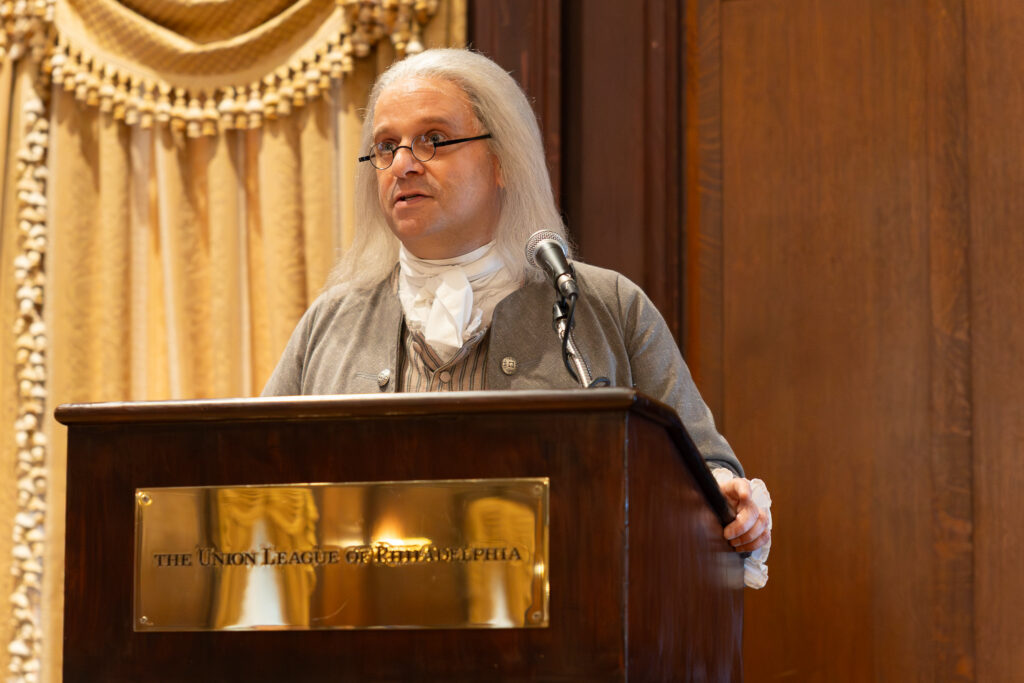 Man dressed in colonial outfit at a podium making a speech.