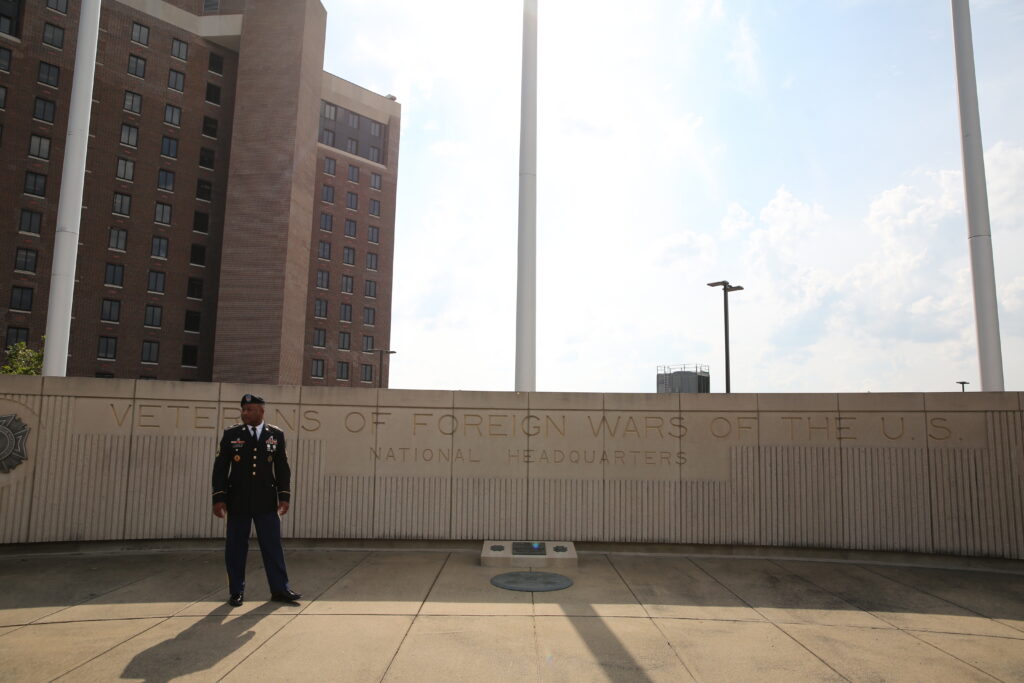 A service member stands proudly in front of the Veterans of Foreign Wars National Headquarters building.