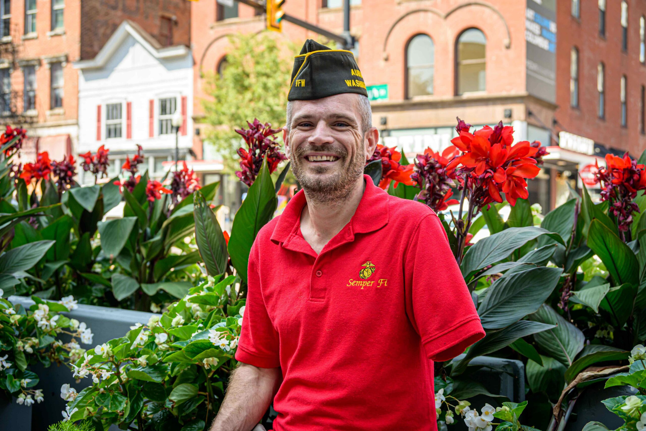 Smiling man in a red shirt and cap sits among vibrant flowers, promoting community engagement and support.