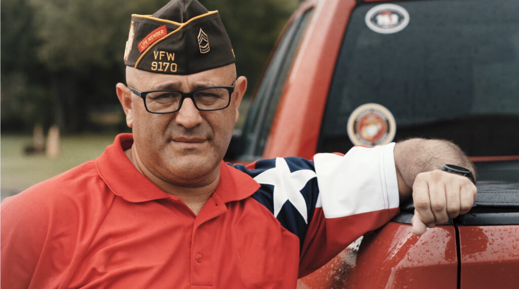 Veteran in a red polo leaning against the bed of a pickup truck
