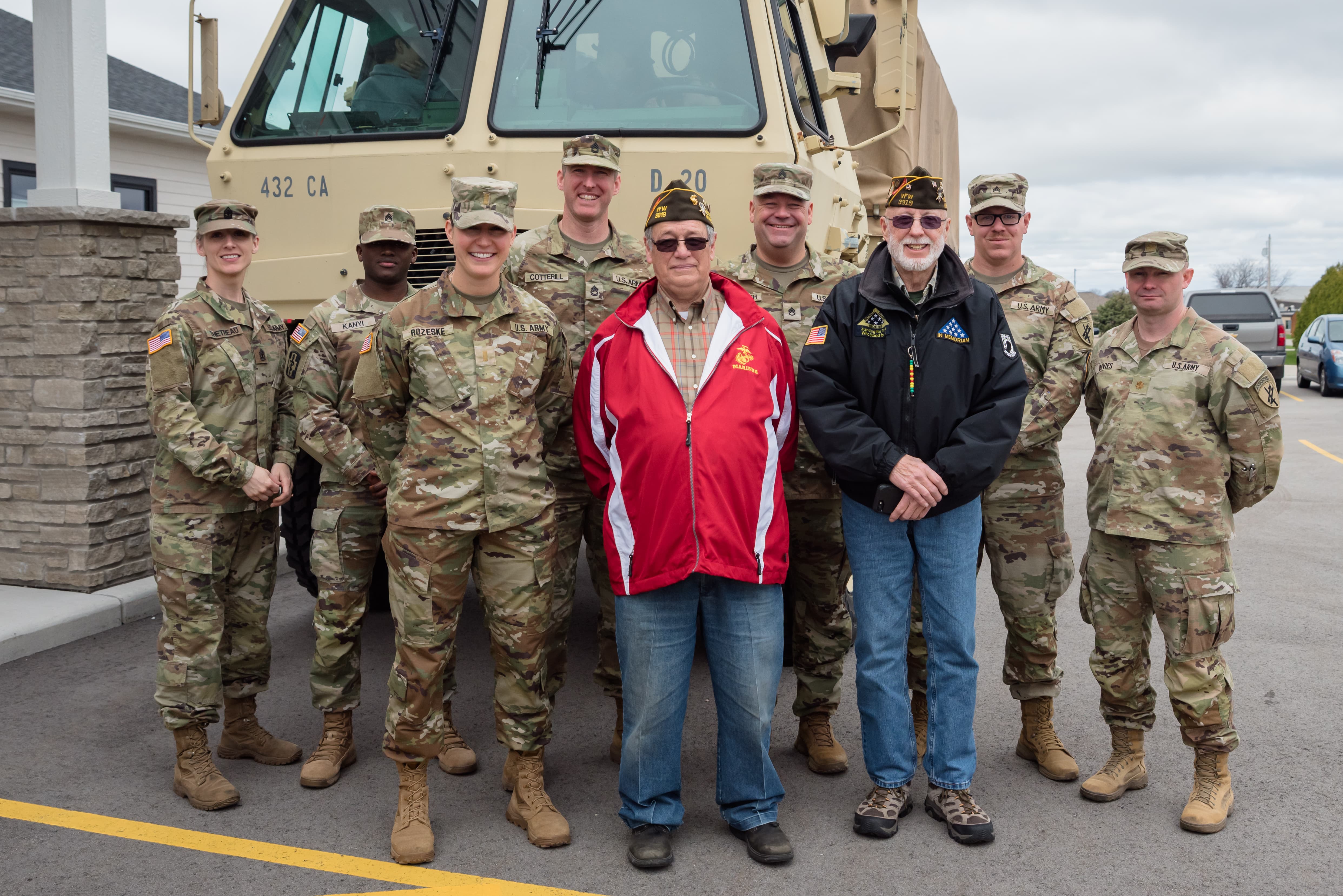 Service members and veterans pose together in front of a military vehicle, showcasing community support and appreciation.