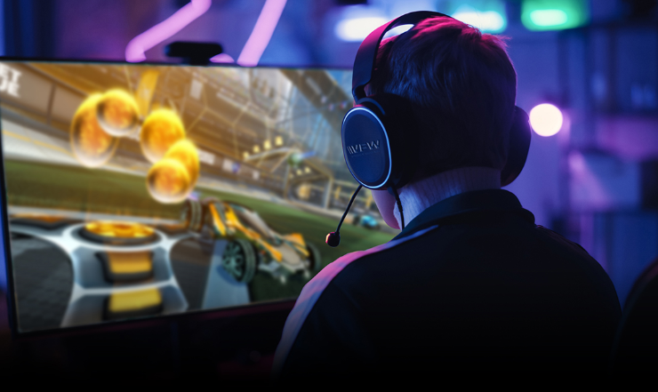 A gamer wearing a headset focuses intently on a vibrant Rocket League match displayed on a large screen.